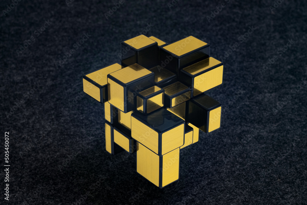 Złota Kostka Rubika typu mirror, przesunięta oś obrotu sprawia, że kostka nabiera nieoczekiwanych geometrycznych kształtów - obrazy, fototapety, plakaty 
