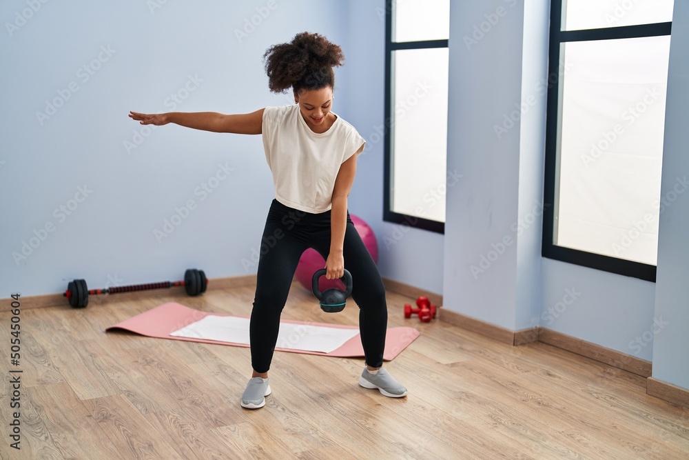 Obraz premium Young african american woman smiling confident training using kettlebell at sport center