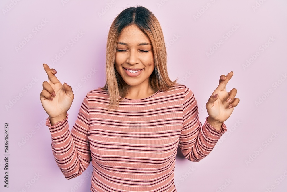 Beautiful hispanic woman wearing casual striped sweater gesturing finger crossed smiling with hope and eyes closed. luck and superstitious concept. Beautiful hispanic woman wearing casual striped sweater gesturing finger crossed smiling with hope and eyes closed. luck and superstitious concept.