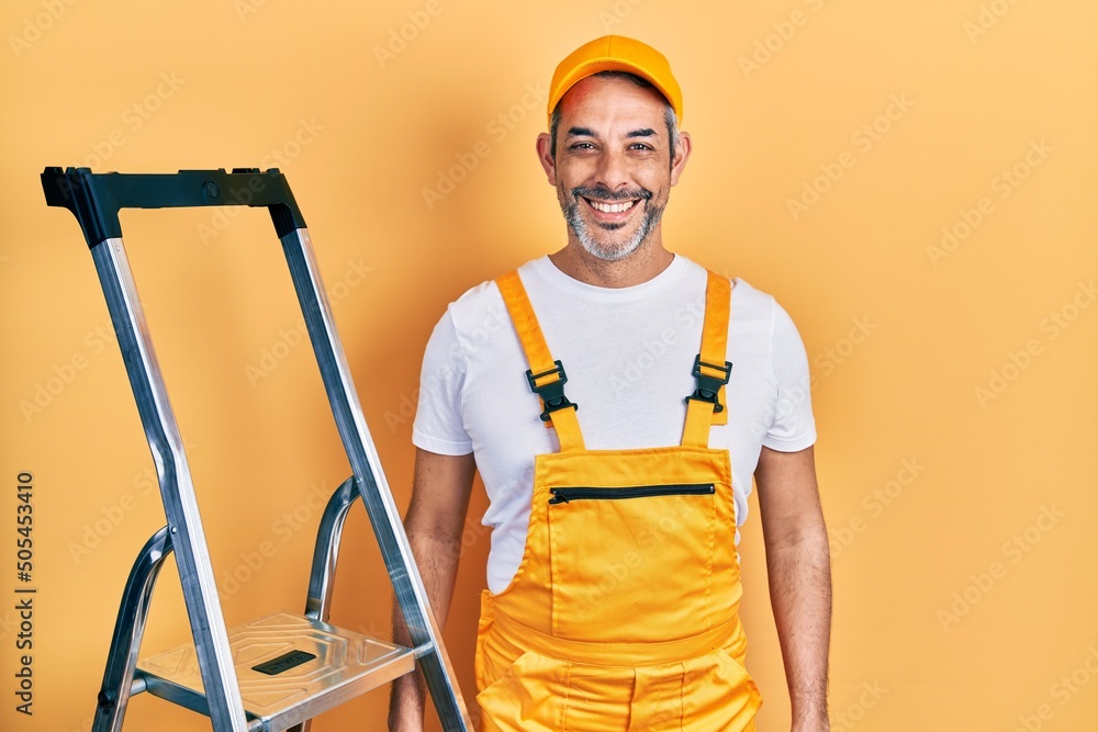 Handsome middle age man with grey hair holding ladder with a happy and cool smile on face. lucky person. Handsome middle age man with grey hair holding ladder with a happy and cool smile on face. lucky person.