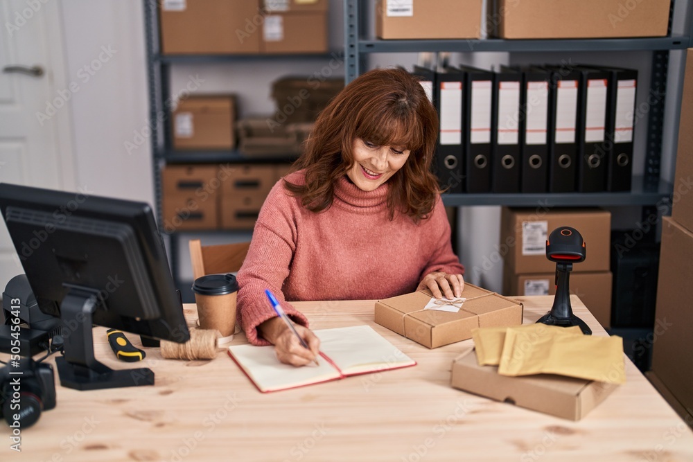 Middle age woman ecommerce business worker writing on book at office Middle age woman ecommerce business worker writing on book at office