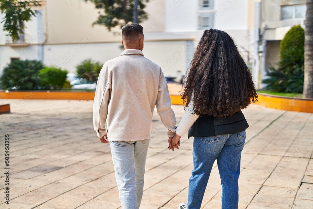Man and woman couple walking on back view with hands together at park Man and woman couple walking on back view with hands together at park