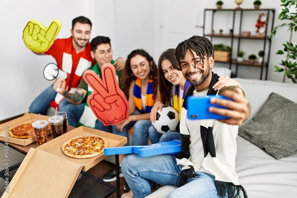Group of young friends watching and supporting soccer match make selfie by the smartphone at home. Group of young friends watching and supporting soccer match make selfie by the smartphone at home.