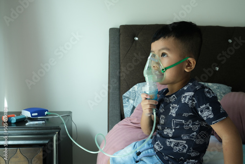 A picture of a boy using home nebulizer machine for treating asthma, bronchitis and illness related to respitory at bed.