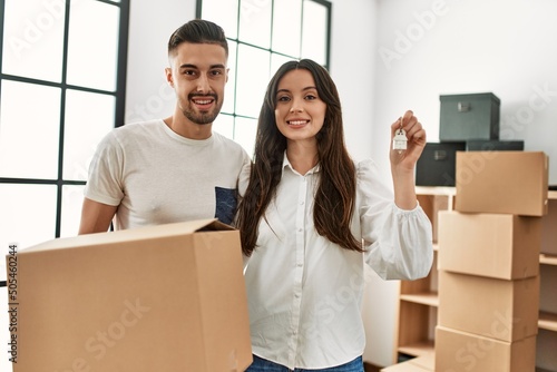 Young hispanic couple smiling happy holding cardboard boxes and key of new home. © Krakenimages.com