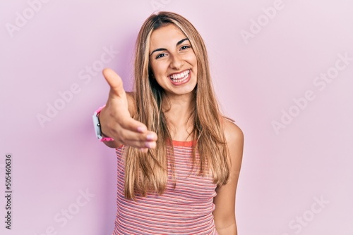 Beautiful hispanic woman wearing casual summer t shirt smiling friendly offering handshake as greeting and welcoming. successful business.