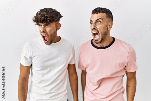 Young gay couple standing over isolated background angry and mad screaming frustrated and furious, shouting with anger. rage and aggressive concept.