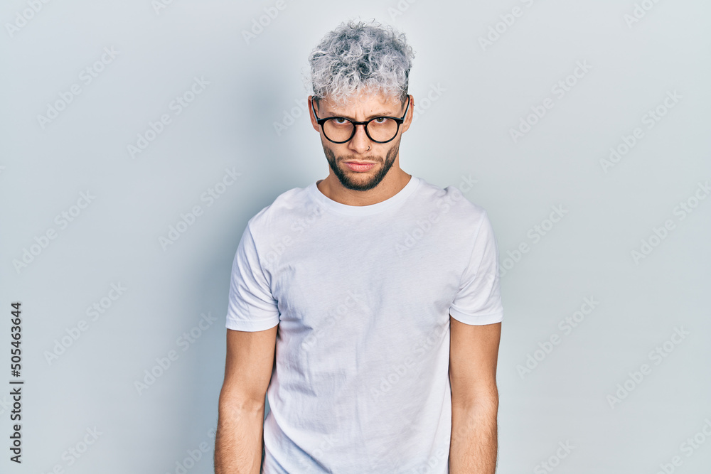 Young hispanic man with modern dyed hair wearing white t shirt and glasses skeptic and nervous, frowning upset because of problem. negative person. Young hispanic man with modern dyed hair wearing white t shirt and glasses skeptic and nervous, frowning upset because of problem. negative person.