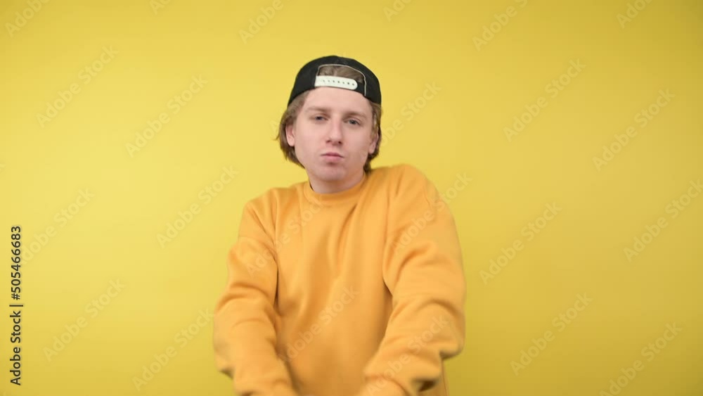 Positive guy in a cap rejoices with raised hands on a yellow background with a smile on his face Positive guy in a cap rejoices with raised hands on a yellow background with a smile on his face