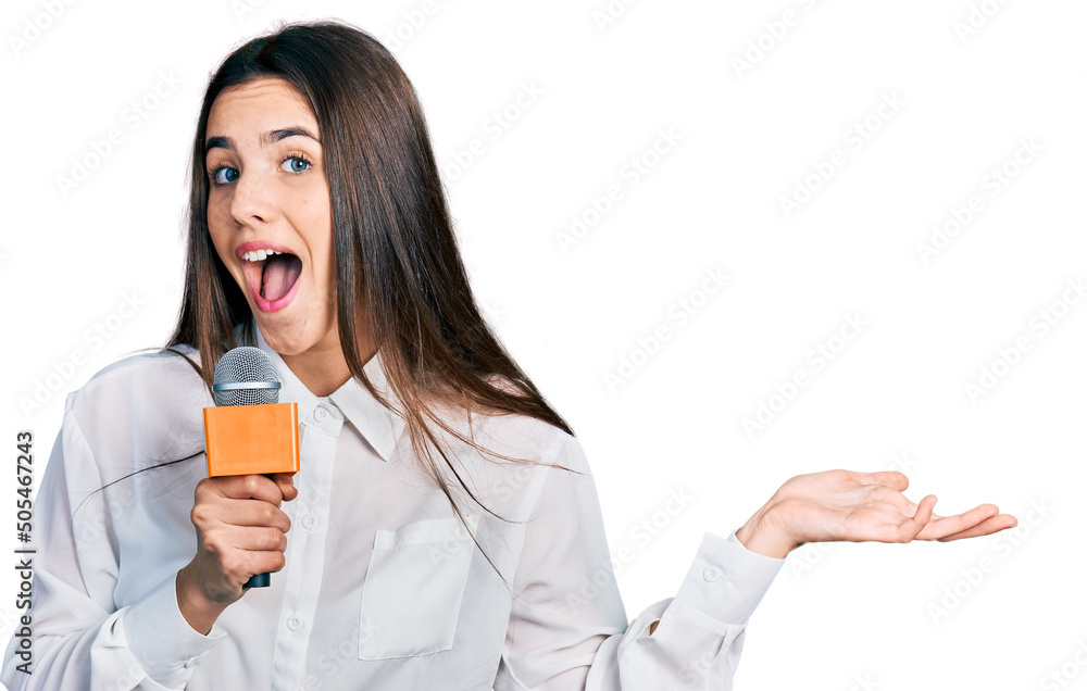 Young brunette teenager holding reporter microphone celebrating achievement with happy smile and winner expression with raised hand Young brunette teenager holding reporter microphone celebrating achievement with happy smile and winner expression with raised hand