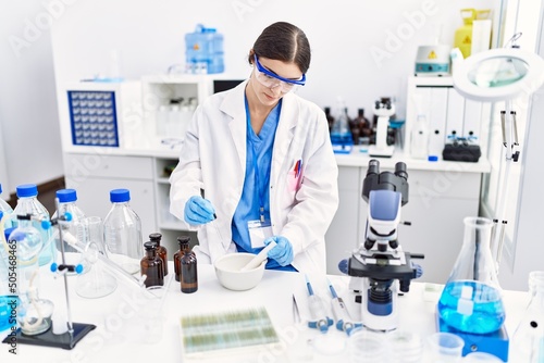 Young hispanic woman wearing scientist uniform working at laboratory