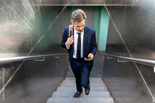 Bilde på lerret Businessman walking upstairs and using smartphone