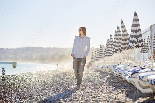 Fototapeta Naklejka Na Ścianę i Meble -  Girls walking on the beach with Blue and White Striped Umbrellas Nice France, French riviera