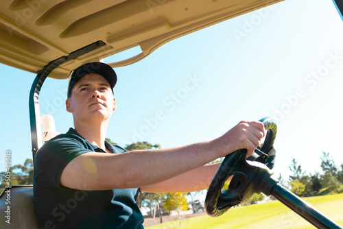 Low angle view of caucasian young man looking away while driving golf cart against clear sky