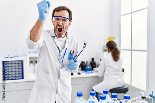 Middle age man working at scientist laboratory annoyed and frustrated shouting with anger  yelling crazy with anger and hand raised
