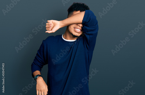 Young african american man wearing casual clothes covering eyes with arm smiling cheerful and funny. blind concept.