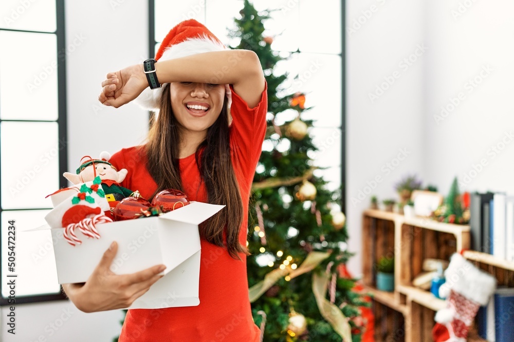 Young brunette woman standing by christmas tree holding decoration smiling cheerful playing peek a boo with hands showing face. surprised and exited Young brunette woman standing by christmas tree holding decoration smiling cheerful playing peek a boo with hands showing face. surprised and exited