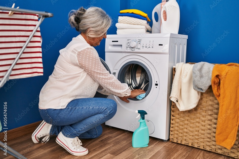 Middle age woman cleaning washing machine at laundry room Middle age woman cleaning washing machine at laundry room