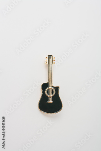 Metallic golden brooch in shape of black guitar, pin on white background. Bijouterie, jewelry for musician, close up