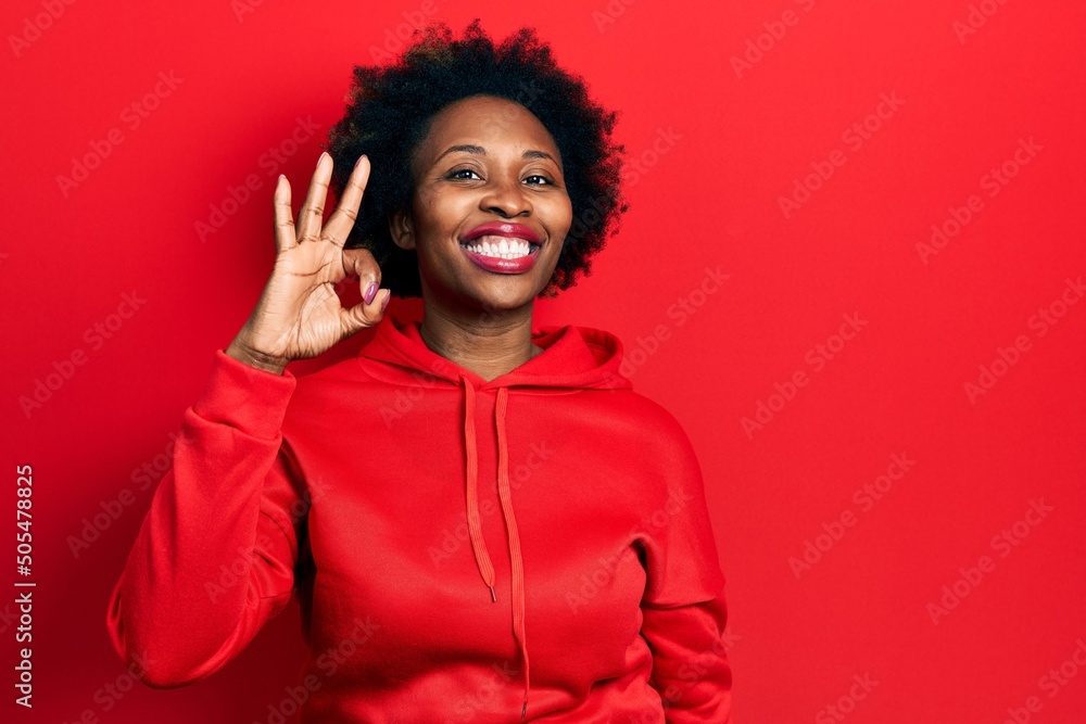 Young african american woman wearing casual sweatshirt smiling positive doing ok sign with hand and fingers. successful expression. Young african american woman wearing casual sweatshirt smiling positive doing ok sign with hand and fingers. successful expression.