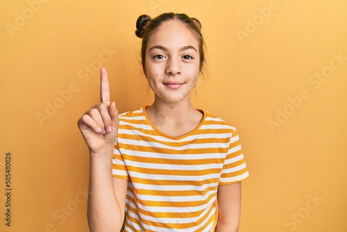 Beautiful brunette little girl wearing casual striped t shirt showing and pointing up with finger number one while smiling confident and happy.