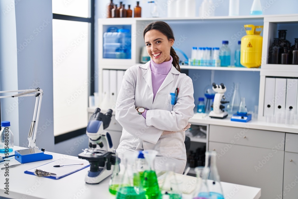 Young brunette woman working at scientist laboratory happy face smiling with crossed arms looking at the camera. positive person. Young brunette woman working at scientist laboratory happy face smiling with crossed arms looking at the camera. positive person.