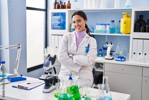 Young brunette woman working at scientist laboratory happy face smiling with crossed arms looking at the camera. positive person.