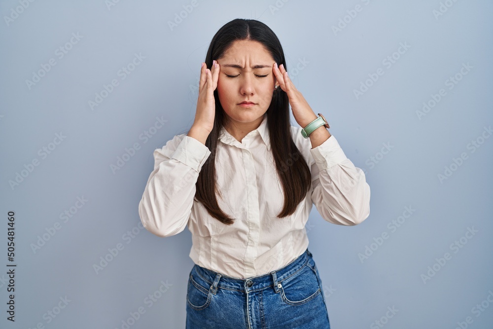 Young latin woman standing over blue background with hand on head, headache because stress. suffering migraine. Young latin woman standing over blue background with hand on head, headache because stress. suffering migraine.