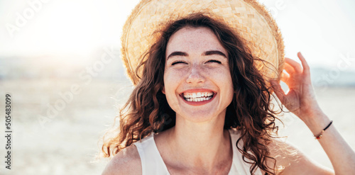 Canvas Print Young joyful woman in white shirt wearing hat smiling at camera on the beach - T
