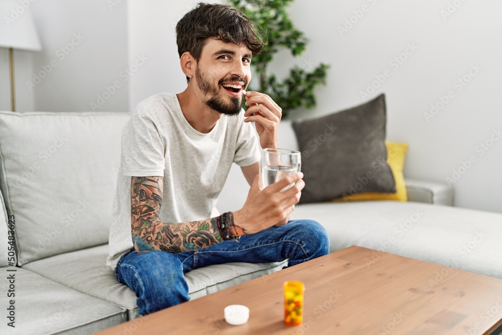 Young hispanic man taking pills sitting on the sofa at home Young hispanic man taking pills sitting on the sofa at home