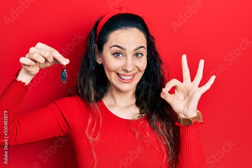 Young hispanic woman holding cockroach doing ok sign with fingers, smiling friendly gesturing excellent symbol