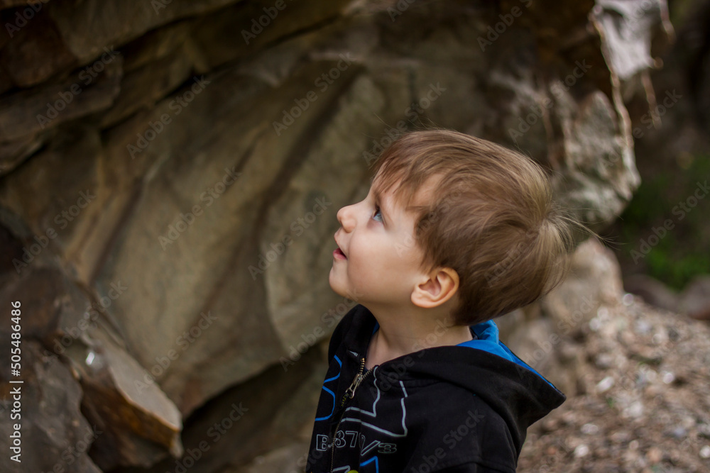 Φωτογραφία A boy-child on the background of a rocky mountain looks at something with curiosity and is surprised