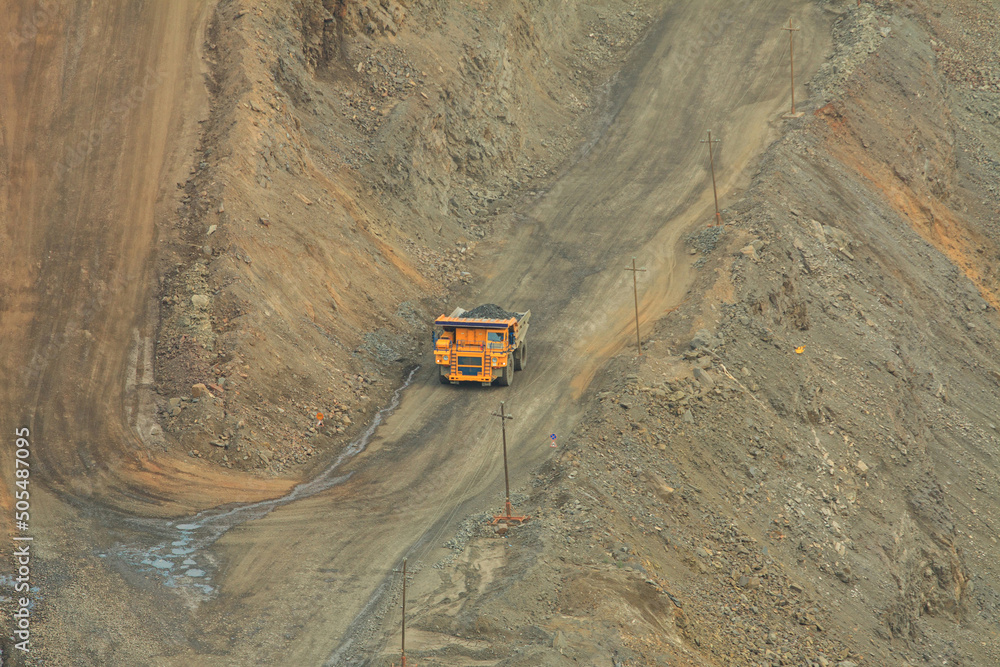 A mining dump truck loaded with iron ore moves along the serpentine of the quarry. The process of open-pit mining. A mining dump truck loaded with iron ore moves along the serpentine of the quarry. The process of open-pit mining.
