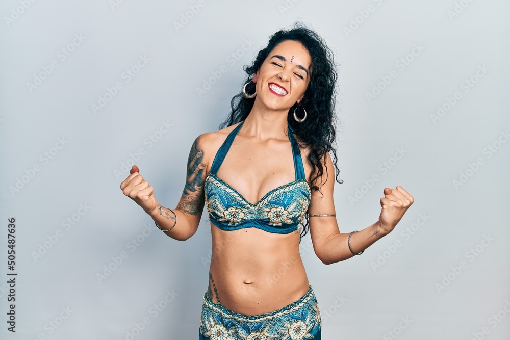 Fototapeta premium Young woman wearing bindi and traditional belly dance clothes very happy and excited doing winner gesture with arms raised, smiling and screaming for success. celebration concept.