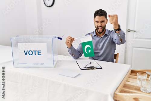 Young handsome man with beard at political campaign election holding pakistan flag annoyed and frustrated shouting with anger, yelling crazy with anger and hand raised