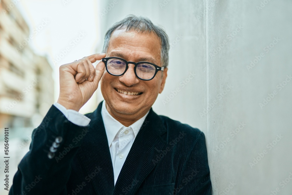 Middle age southeast asian man standing and smiling confident holding glasses leaning on the wall Middle age southeast asian man standing and smiling confident holding glasses leaning on the wall