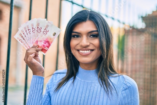 Beautiful hispanic woman smiling confient holding 20 shekels banknotes at the city photo