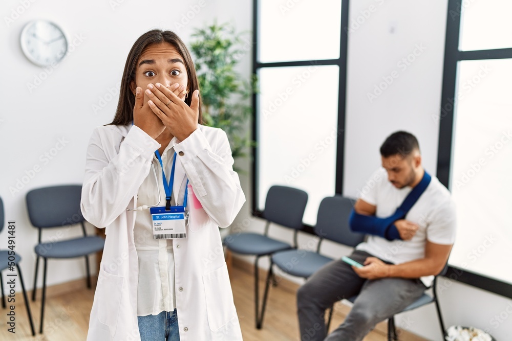 Young asian doctor woman at waiting room with a man with a broken arm shocked covering mouth with hands for mistake. secret concept. Young asian doctor woman at waiting room with a man with a broken arm shocked covering mouth with hands for mistake. secret concept.