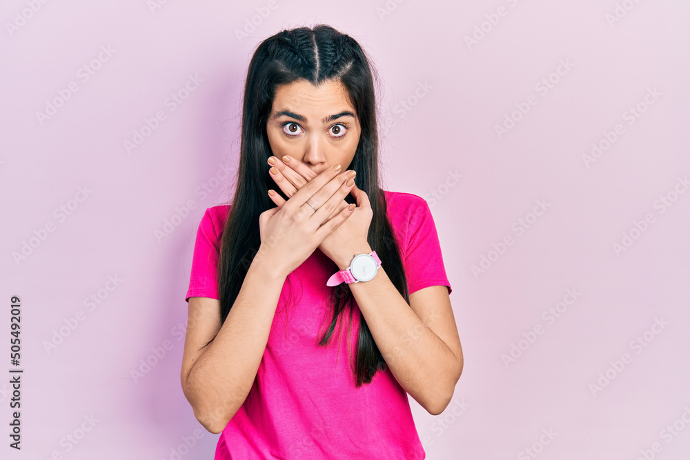 Young hispanic girl wearing casual pink t shirt shocked covering mouth with hands for mistake. secret concept. Young hispanic girl wearing casual pink t shirt shocked covering mouth with hands for mistake. secret concept.