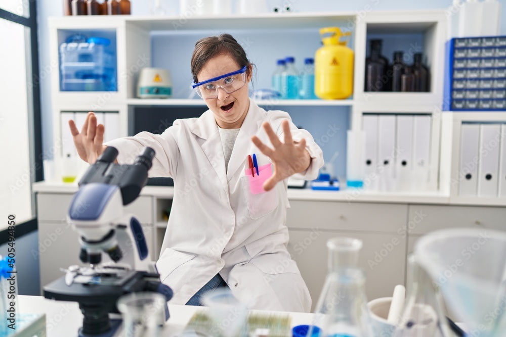 Hispanic girl with down syndrome working at scientist laboratory doing stop gesture with hands palms, angry and frustration expression Hispanic girl with down syndrome working at scientist laboratory doing stop gesture with hands palms, angry and frustration expression