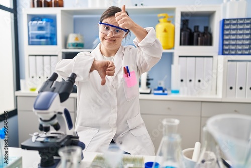 Hispanic girl with down syndrome working at scientist laboratory doing thumbs up and down, disagreement and agreement expression. crazy conflict
