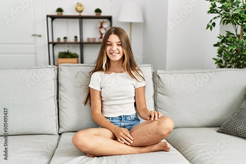 Young brunette teenager sitting on the sofa at home winking looking at the camera with sexy expression, cheerful and happy face.