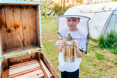 Portrait of boy beekeeper in a protective suit holds a smoker in his hands. Beekeeper's tool. Inspection of wooden beehives. beekeeping.
