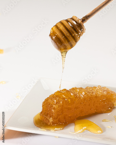 honey dripping from honey dipper and onto a honey comb on a white plexiglas background