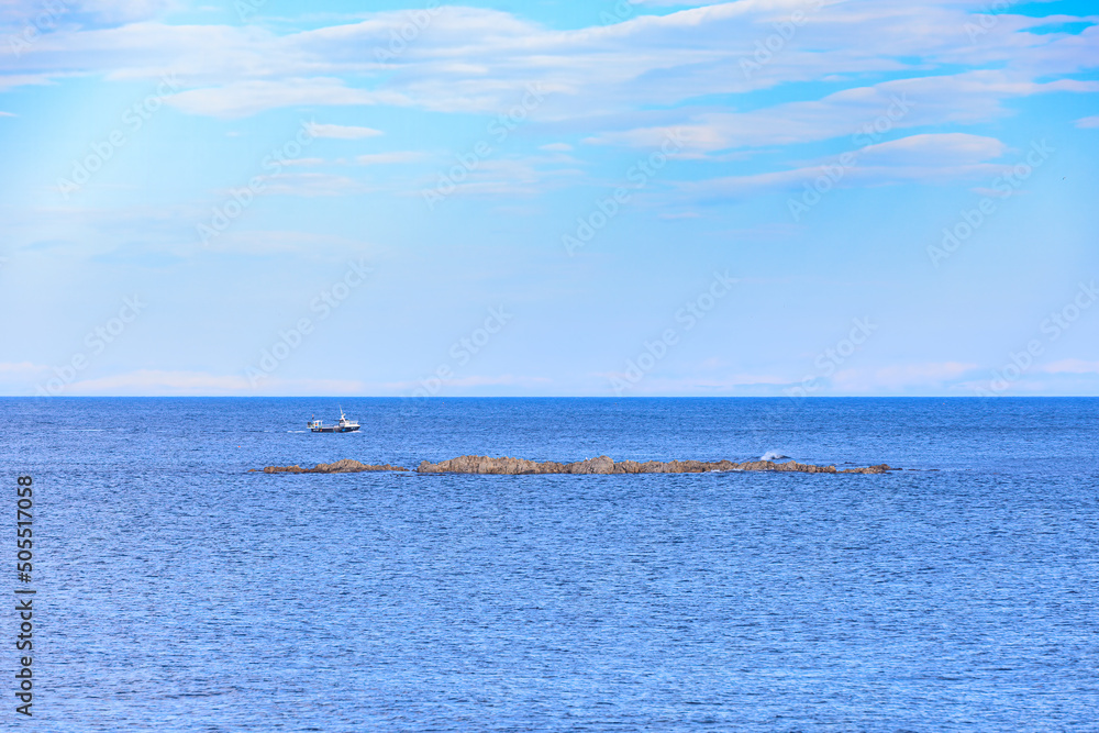 A scenic view of a bay with a rocky island and a fishing boat under a majestic blue sky and some white clouds