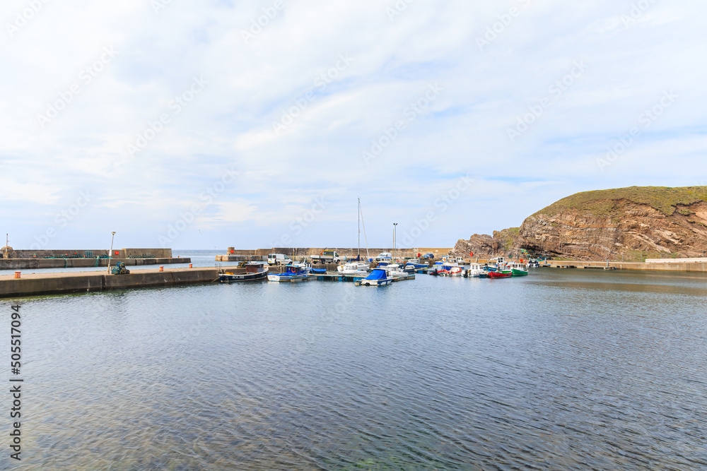 A scenic view of a scottish port marina with fishing and leisure boat along some cliff A scenic view of a scottish port marina with fishing and leisure boat along some cliff