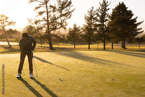 Full length of caucasian young man hitting golf ball with club against trees and clear sky at sunset photo