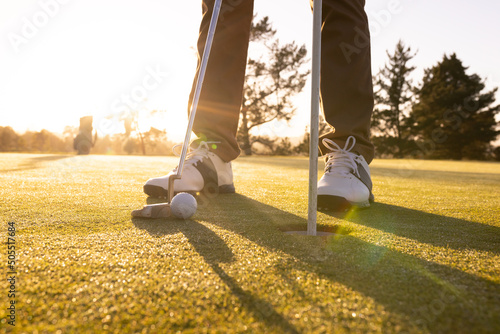 Low section of caucasian young man with club, ball and flagstick in hole standing at golf course photo