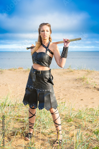 female fighter wearing dark leather armor with iron falchion in her hand is standing on the seaside photo