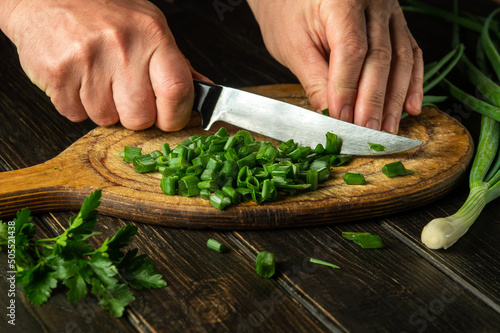 Slicing green onions on a cutting board with a knife for cooking vegetarian food. Peasant dish